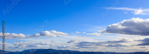 Blue sky background with scattered clouds over mountains silhouette. Aerial, panoramic photo banner