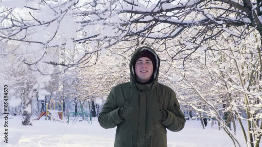 Snow falls from the branch. A man covers his head with a hood. Slow motion. Snow falls from the branch. A man covers his head with a hood. Slow motion.