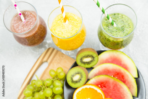 Tropical Healthy Smoothie and a plate of fresh fruit  kiwi  orange  watermelon and grape on a light table against a blue wooden wall  top view. Diet  Detox  Healthy Dessert Concept