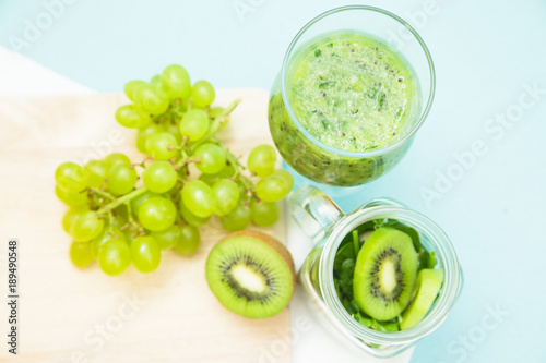 Preparing green smoothie with kiwi, banana, grapes and spinach on a wooden cutting board, light blue background, top view Diet, Fitness, Dessert Concept