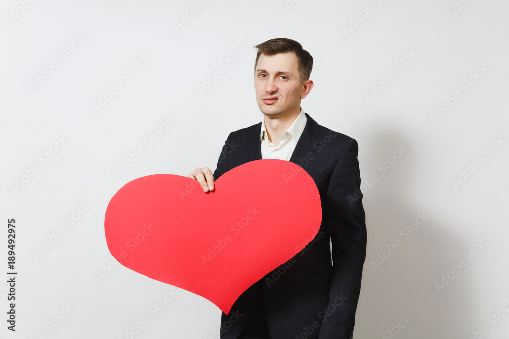 Young stunned shocked upset sad man in suit holding big red heart isolated on white background. Copy space for advertisement. St. Valentine's Day, International Women's Day, birthday, holiday concept. Young stunned shocked upset sad man in suit holding big red heart isolated on white background. Copy space for advertisement. St. Valentine's Day, International Women's Day, birthday, holiday concept.