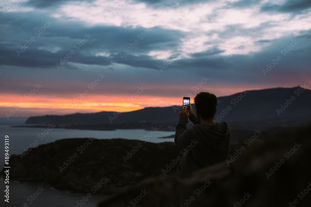 Lonely figure of tourist or traveler that stands on top of cliff or mountain, epic travel destination for 2018, captures beautiful sunset or sunrise shots on smartphone camera