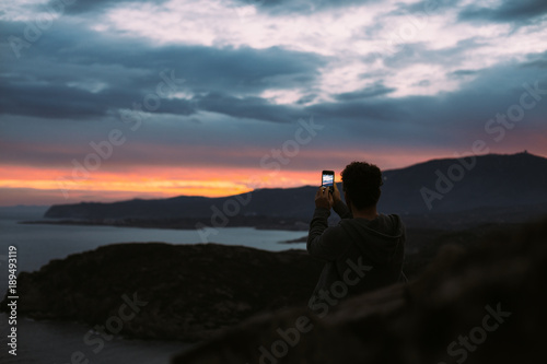 Lonely figure of tourist or traveler that stands on top of cliff or mountain, epic travel destination for 2018, captures beautiful sunset or sunrise shots on smartphone camera © BublikHaus