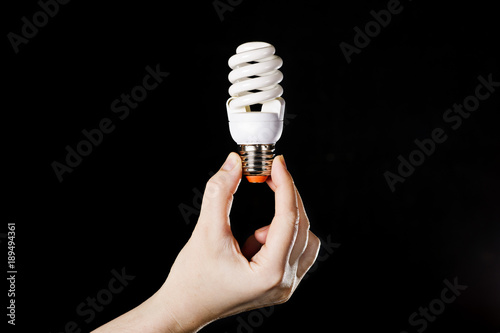 energy saving lamp in hands on a black background