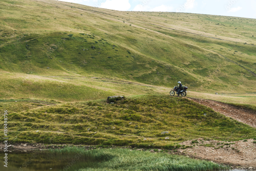Obraz premium Motorcyclist on a mountainous road, cold overcast weather. Extreme sport, active lifestyle, adventure touring concept. High mountains, dirt roads. enduro off road touring