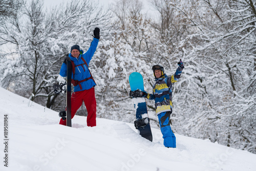 Happy snowboarders are standing in the forest after snowfall