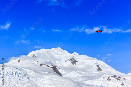 Small red plane flying among clouds over snow peaks and glaciers, Hald Moon island, Antarctic peninsula