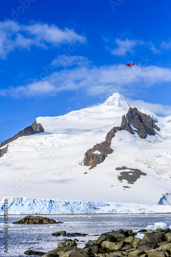 Small red plane flying over snow peaks, glaciers and sea fjord, Hald Moon island,  Antarctic peninsula © vadim.nefedov