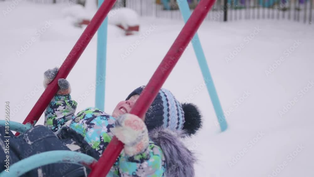 A small child is playing in winter Park. A child on a swing. A Sunny winter day. Fun and games in the fresh air.