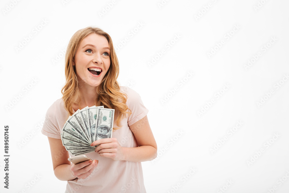 Excited young lady holding money using mobile phone. Excited young lady holding money using mobile phone.