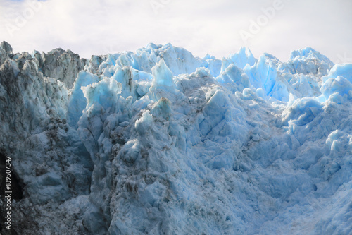 ostre krawędzie czoła lodowca w kolorze biało niebieskim w zbliżeniu z zachmurzonym niebem w tle
