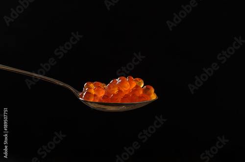 Photos red caviar in a silver teaspoon on a black background