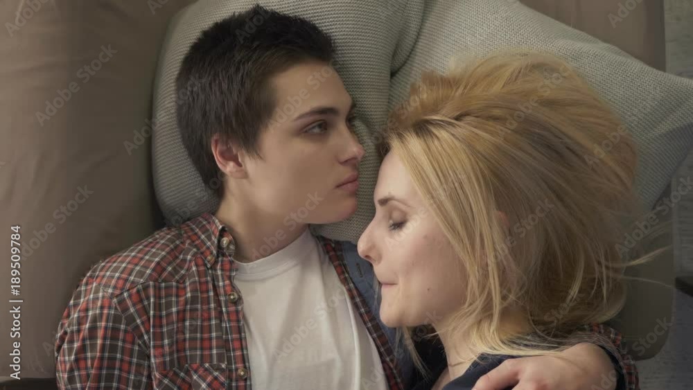 Two young lesbian girls are lying on the bed, a girl with short hair kisses her partner in the forehead, an LGBT family concept, they sleep. 60 fps Stock ビデオ | Adobe Stock 
