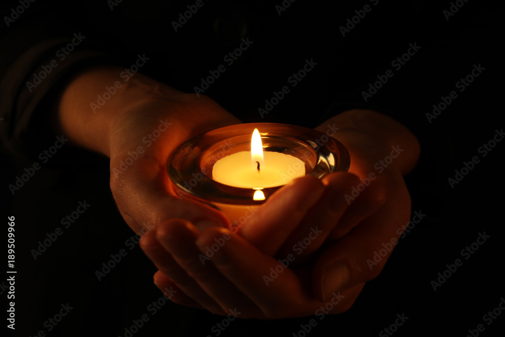 Young woman holding burning candle in darkness Young woman holding burning candle in darkness