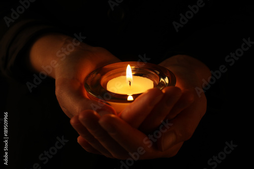Young woman holding burning candle in darkness