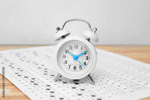 Alarm clock and test sheet on table, closeup. Preparation for exam