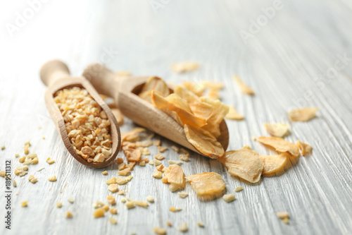 Scoops with granulated dried garlic and flakes on wooden background