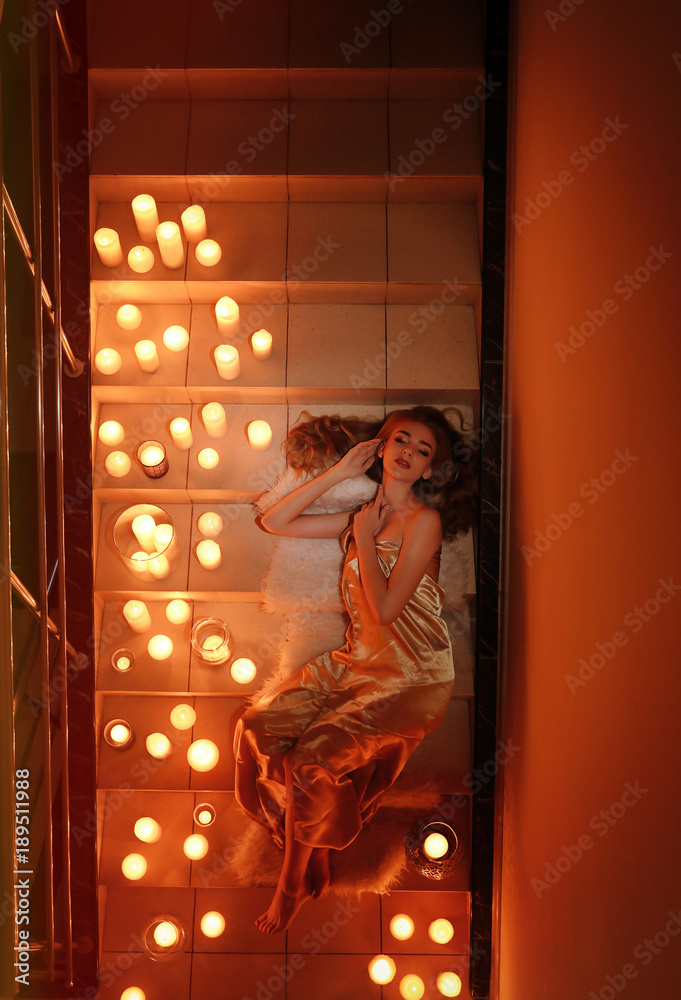 Fototapeta premium Beautiful young woman lying on stairs with burning candles