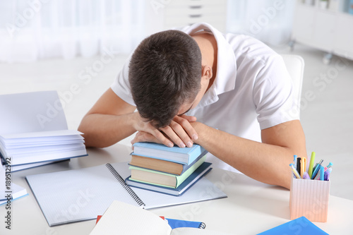 Tired student sleeping on stack of books at his desk. Preparing for exam