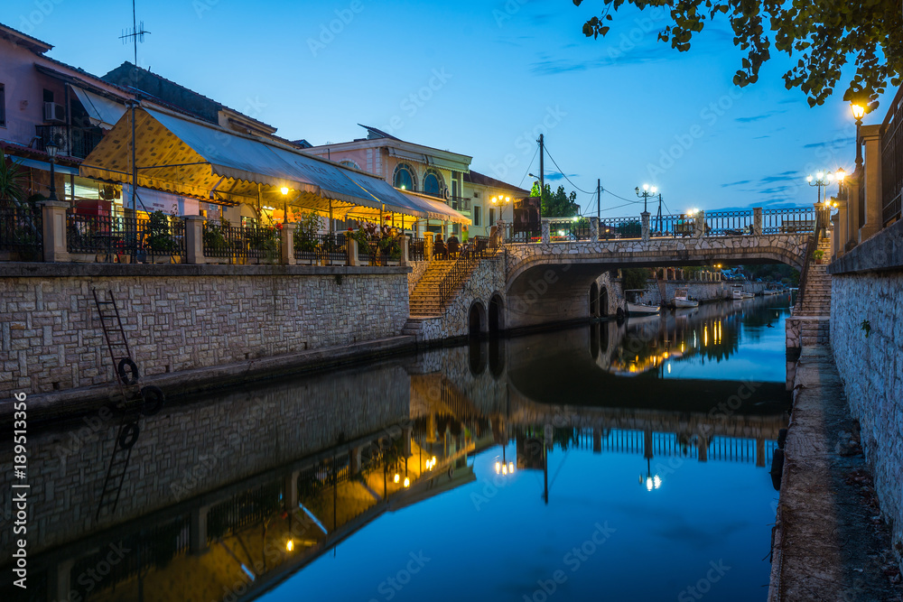 Night scenic view on the bridge above small local river at center of small town with cafe, bar and restaurant on the waterfront.