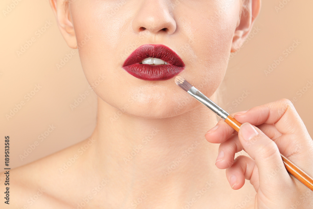 Professional visage artist applying makeup on woman's face on color background
