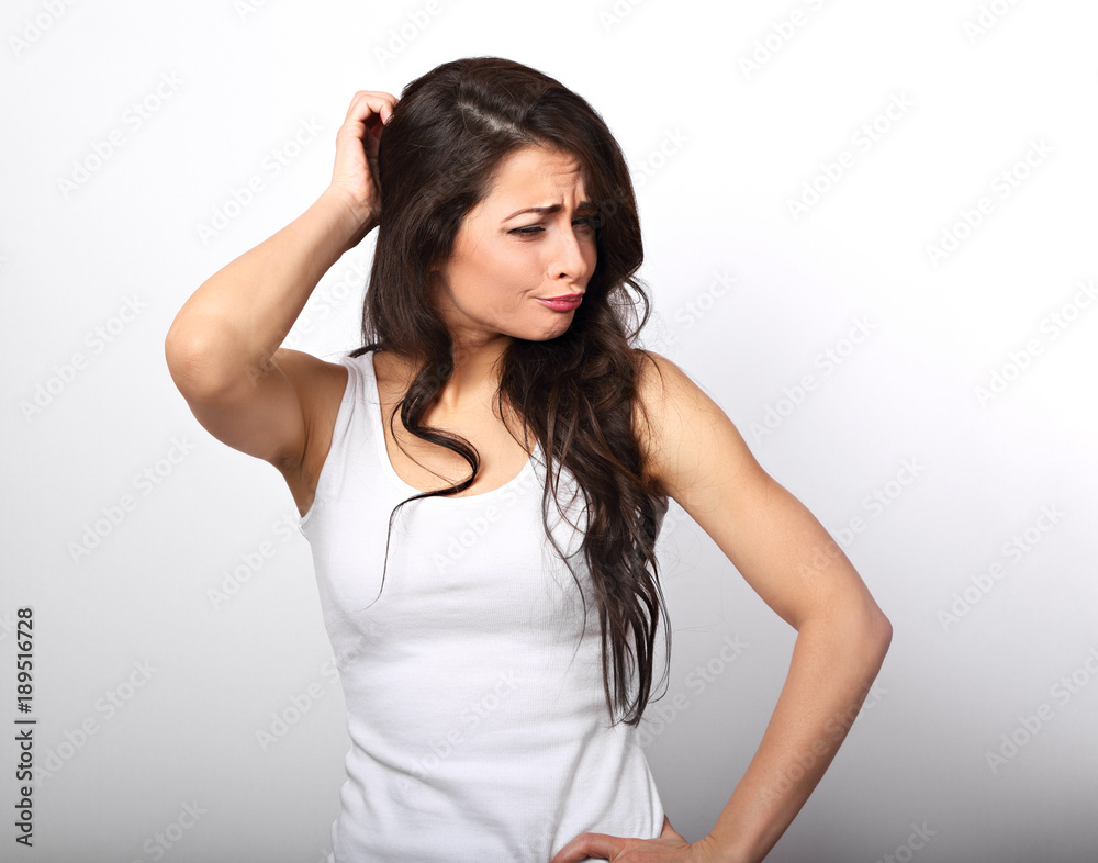 Confusion unhappy brunette woman thinking and scratching the head in white t-shirt on white copy space background Confusion unhappy brunette woman thinking and scratching the head in white t-shirt on white copy space background