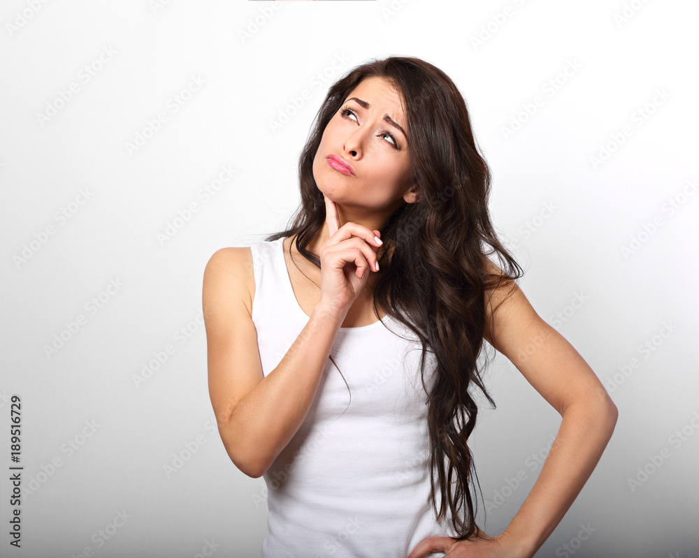 Confusion grimacing brunette woman thinking and looking up in white t-shirt on white copy space background Confusion grimacing brunette woman thinking and looking up in white t-shirt on white copy space background
