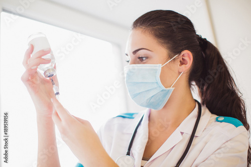 Side view of the positive young nurse who is dialing medicine into the syringe indoors