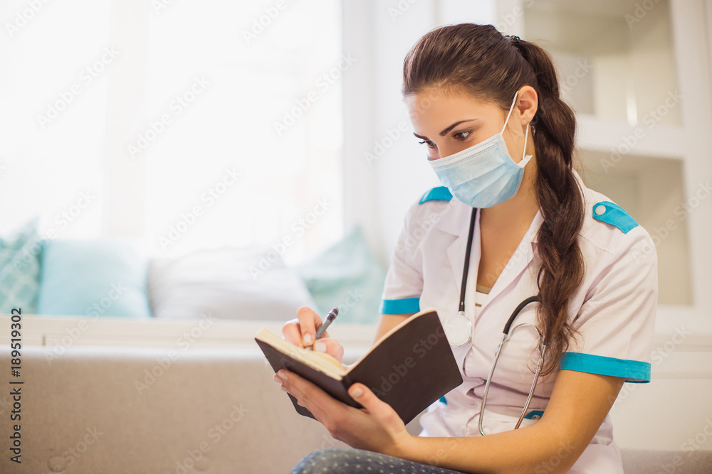 Portrait of the cheerful young doctor who is sitting on a sofa in the room and writing in a notebook Portrait of the cheerful young doctor who is sitting on a sofa in the room and writing in a notebook