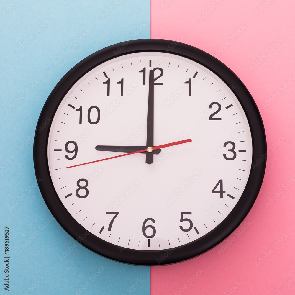 Big wall clock isolated on blue and rose background. Nine o'clock. Big wall clock isolated on blue and rose background. Nine o'clock.