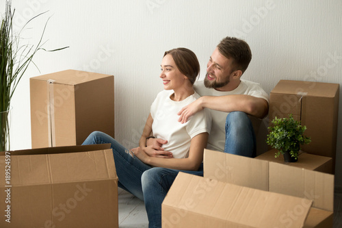 Young couple embracing looking forward to future in new home after moving in relocation, happy smiling man and woman homeowners holding hands dreaming of changes sitting on floor with boxes together © fizkes