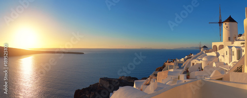 Sunset over Santorini island in Greece. Traditional church, apartments and windmills in Oia village.