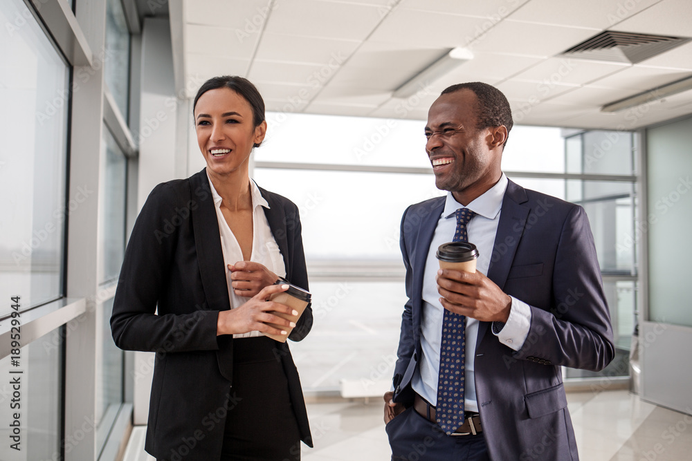 Pause at work. Joyful successful young skilled businesspeople are standing in light office and enjoying hot coffee. They are laughing while talking to each other Pause at work. Joyful successful young skilled businesspeople are standing in light office and enjoying hot coffee. They are laughing while talking to each other