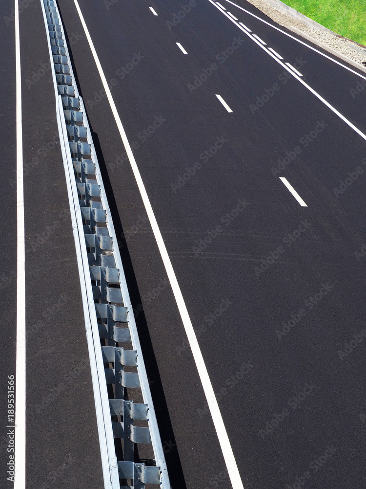 Asphalted highway. Empty motorway. High-speed road of the city. Barrier, guarding rail. Perspective, convergence, vertical top view. Runoff, green grass on the roadside Asphalted highway. Empty motorway. High-speed road of the city. Barrier, guarding rail. Perspective, convergence, vertical top view. Runoff, green grass on the roadside