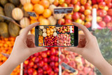 Girl with smartphone taking pictures of fruits on marketplace for her blog