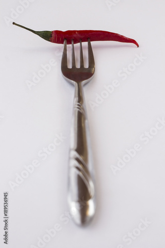 Chili pepper on the fork. White background. Vertically.