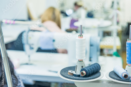 Fototapeta Naklejka Na Ścianę i Meble -  Spools of thread in the sewing equipment with blurred working tailors on background. The concept of sewing production. Selective focus, space for text.