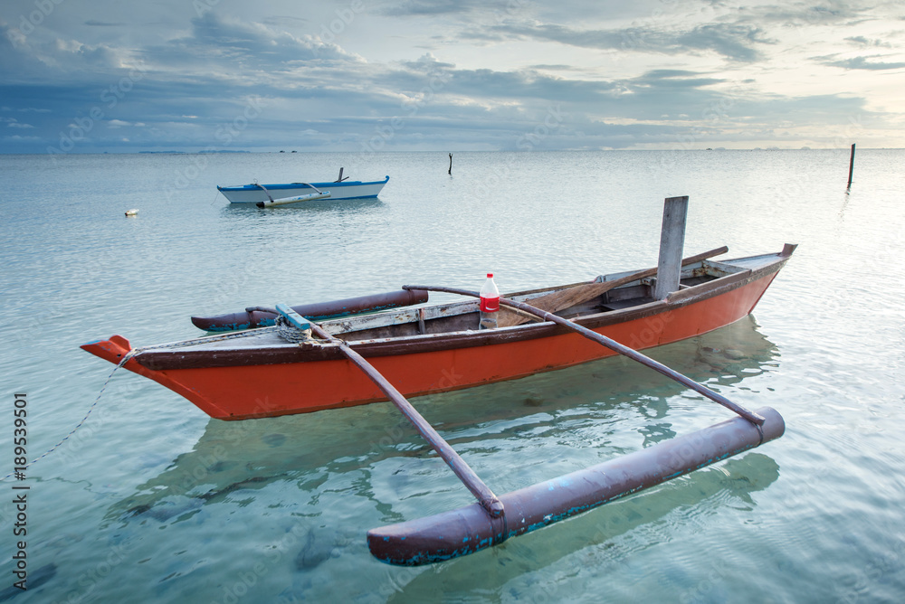 Traditional fishing Canoe floating on clean sea water during sunrise.