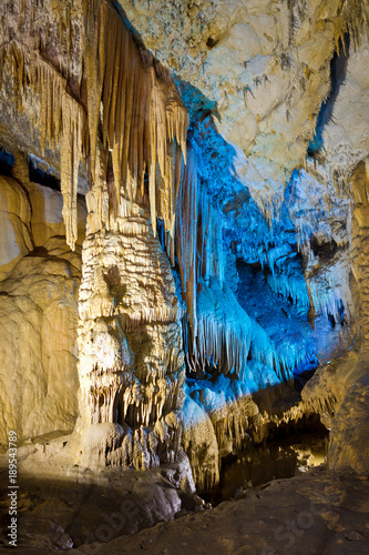 Beautiful speleothem stalagnata, stalactites, stalagmites in natural cave illuminated by color lights