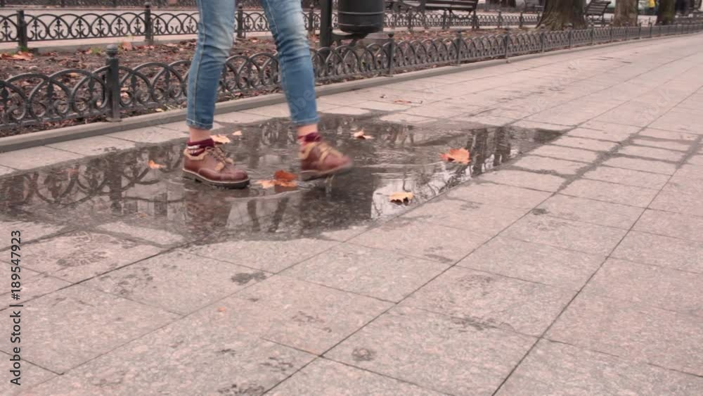 Brown leather boots walk in a puddle with fallen leaves. Close up of cute woman shoes in autumn streets background. Brown leather boots walk in a puddle with fallen leaves. Close up of cute woman shoes in autumn streets background.