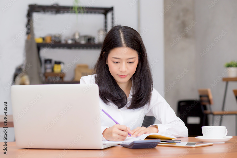 Business asian woman writing on notebook on table with laptop, girl work at coffee shop, freelance business concept. Business asian woman writing on notebook on table with laptop, girl work at coffee shop, freelance business concept.