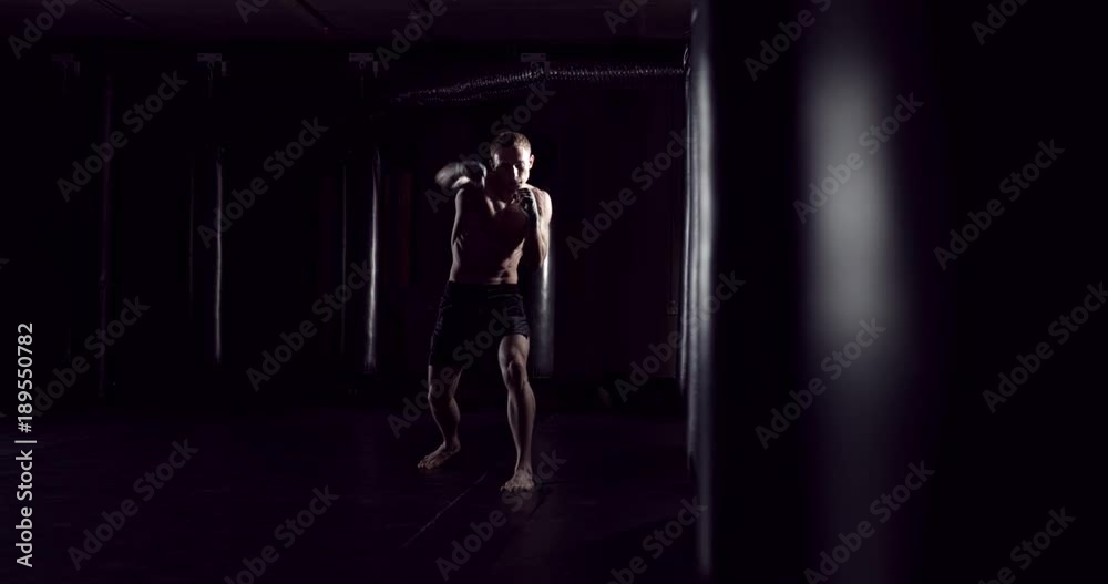 Kickboxer shadow boxing as exercise for the fight. Fighter training punching. Boxing in the darknes. Young boxer training in the gym Kickboxer shadow boxing as exercise for the fight. Fighter training punching. Boxing in the darknes. Young boxer training in the gym