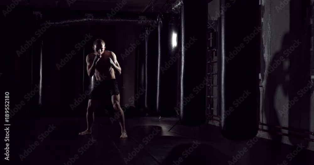 Kickboxer shadow boxing as exercise for the fight. Fighter training punching. Boxing in the darknes. Young boxer training in the gym Kickboxer shadow boxing as exercise for the fight. Fighter training punching. Boxing in the darknes. Young boxer training in the gym