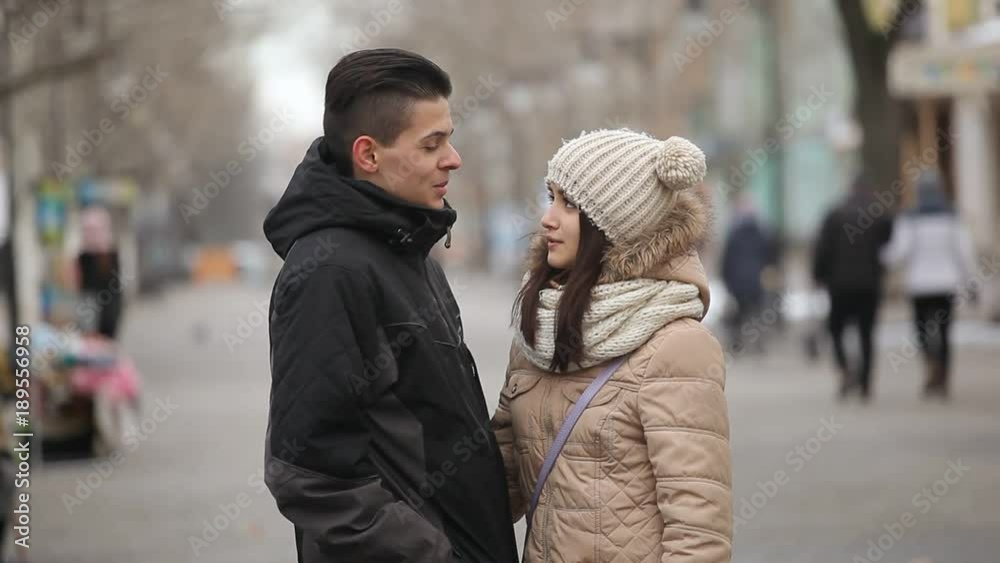 A cheery view of a young happy man and his beautiful girlfriend whispering in a love bla-bla-blah on an arty alley in winter. A cheery view of a young happy man and his beautiful girlfriend whispering in a love bla-bla-blah on an arty alley in winter.