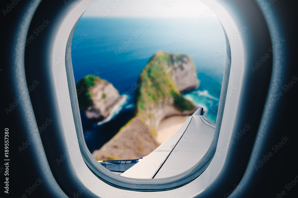 Airplane is flying over blue sea. Tropical beach ocean landscape. View from plane window