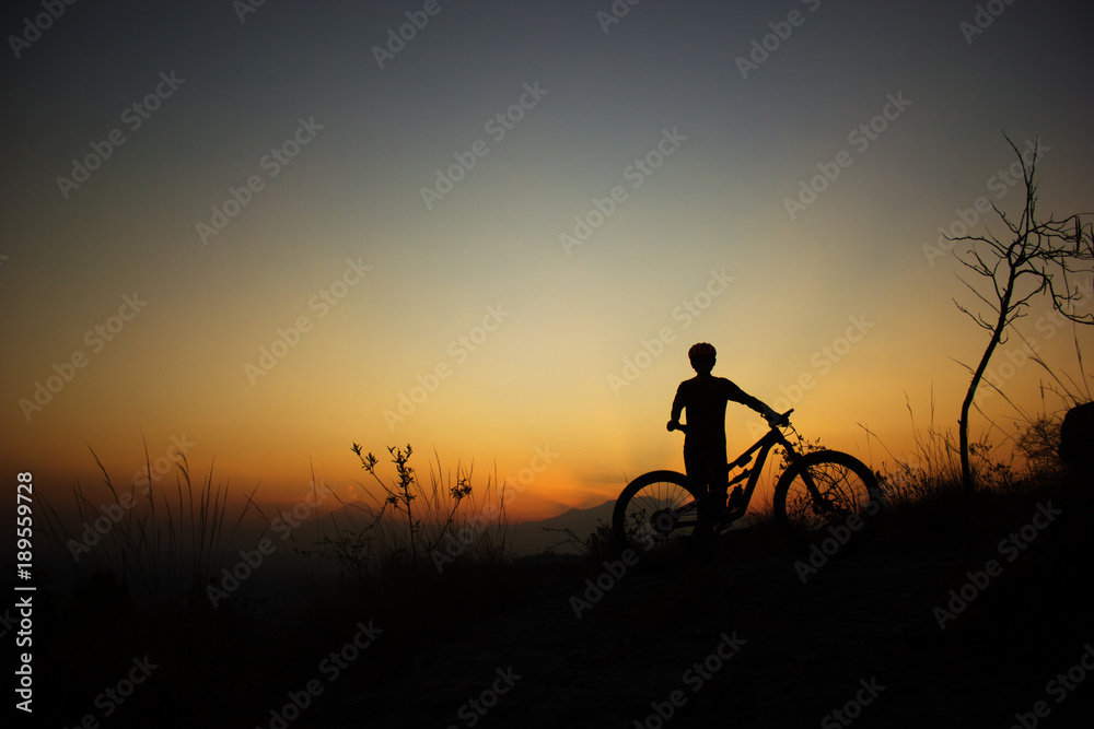 silhouette of a male mtb rider standing at sunset with volcanoes in the background