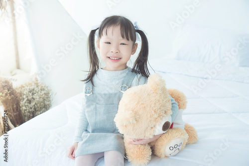 Little asian girl smiling while hugging stuffed bear on bed