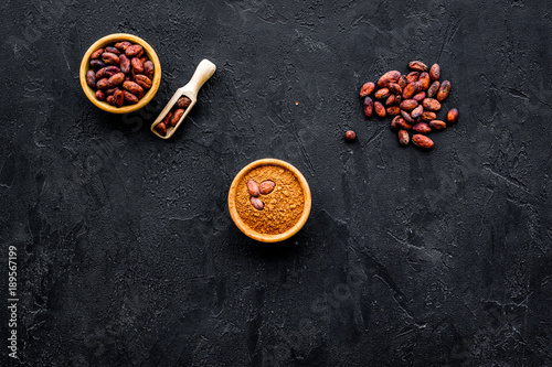 Cocoa powder in bowl and cocoa beans on black background top view copy space. Popular ingregients for sweets, bakery, drinks