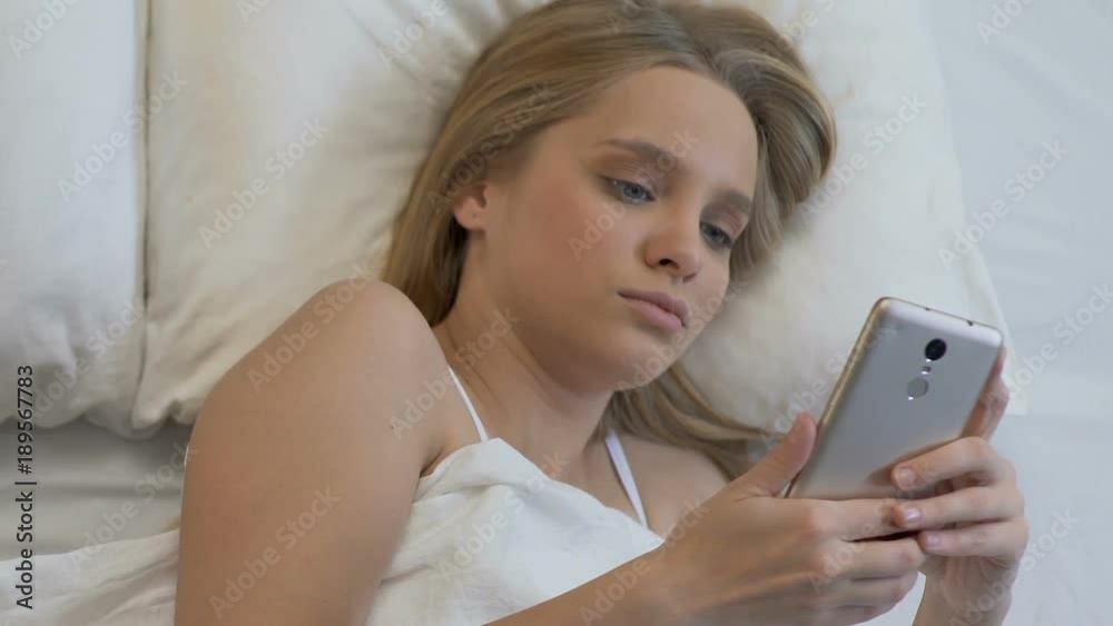 Pretty girl ordering food online by phone application in bed, messaging friend Pretty girl ordering food online by phone application in bed, messaging friend