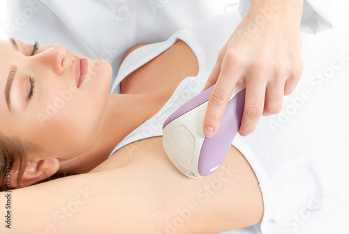 Beautician giving epilation laser treatment to woman on underarm